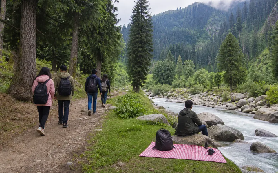 Travellers walking on a forest path and relaxing beside a mountain stream in a Kashmir-style valley