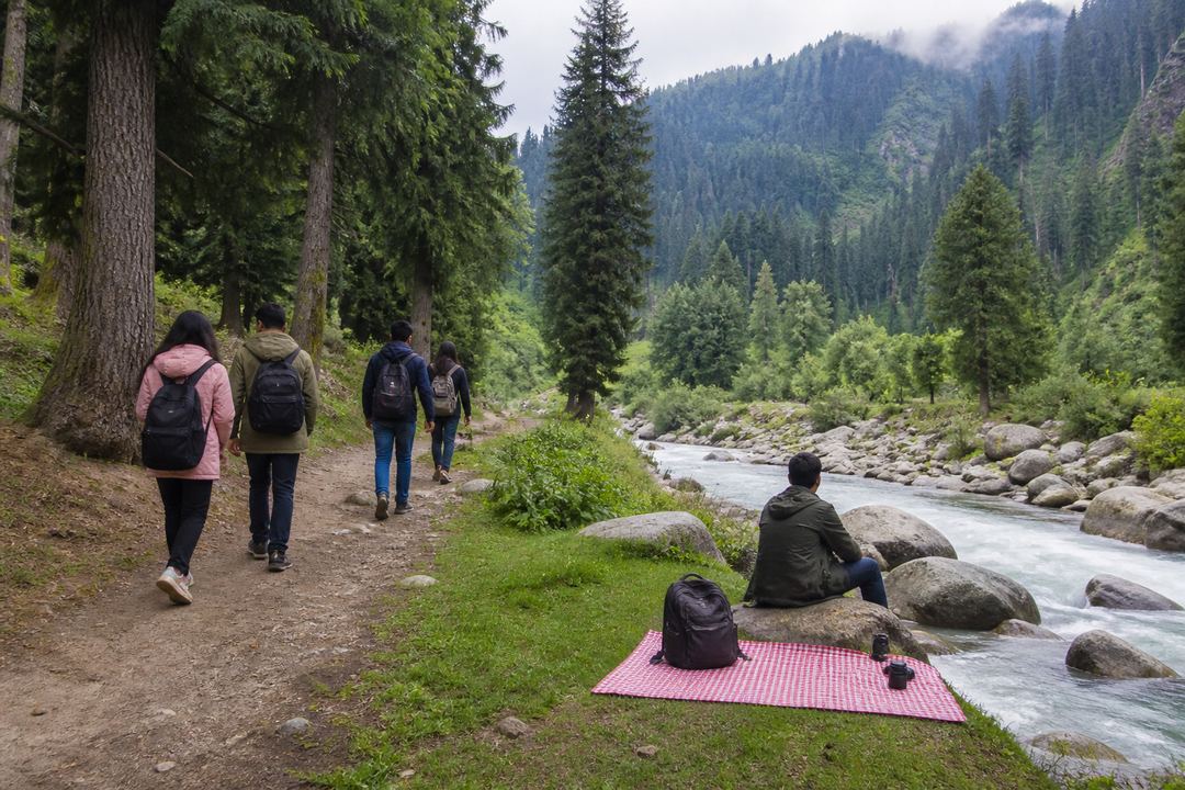 Travellers walking on a forest path and relaxing beside a mountain stream in a Kashmir-style valley