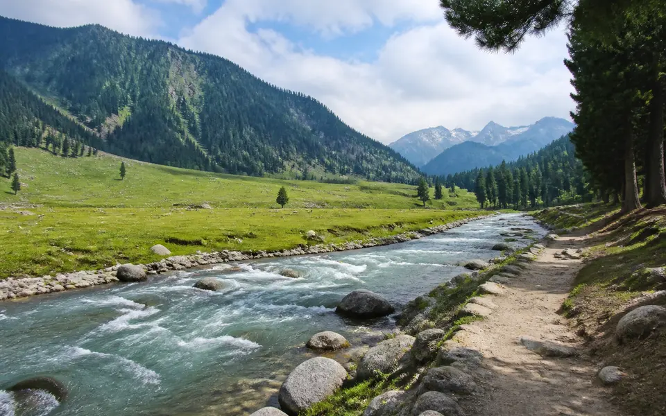 Calm stretch of the Sindh River near Sonamarg with a riverside path, flat meadow and distant mountains.