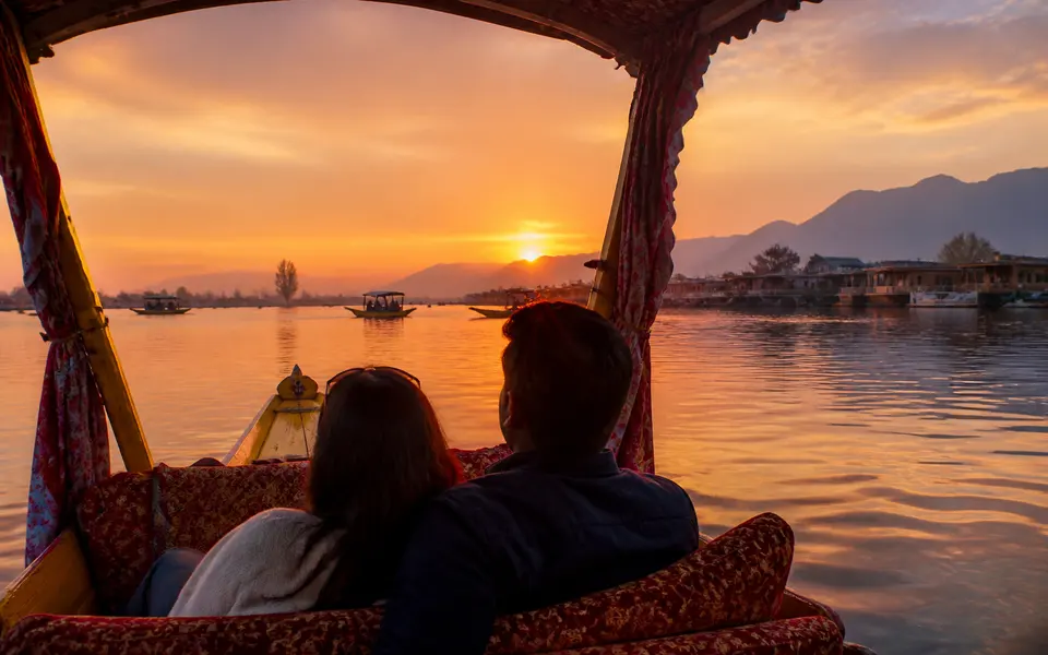 Couple on a shikara during sunset on Dal Lake with golden light reflecting on the water.