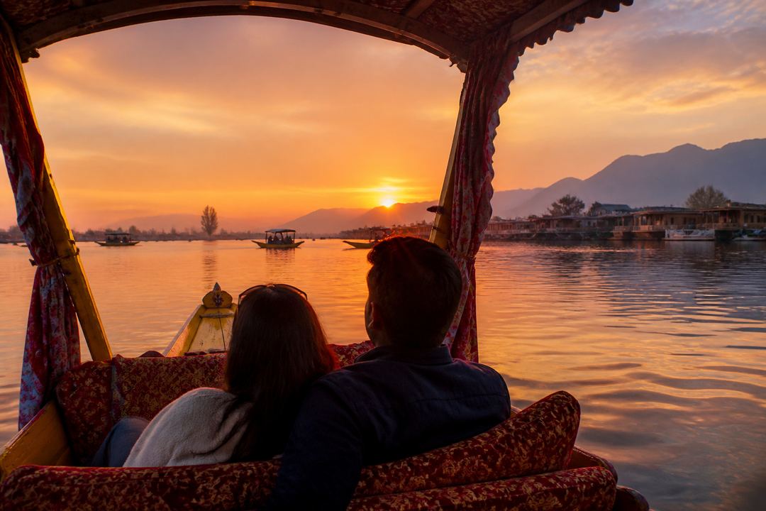Couple on a shikara during sunset on Dal Lake with golden light reflecting on the water.