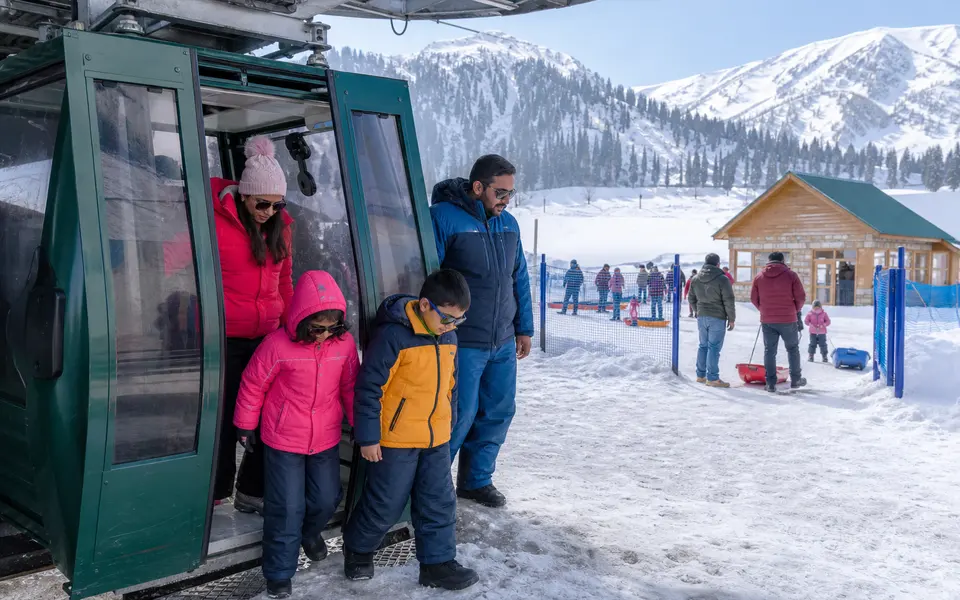 Indian family in winter clothing stepping out of a gondola cabin at Kongdori station with snow and mountain views around them.