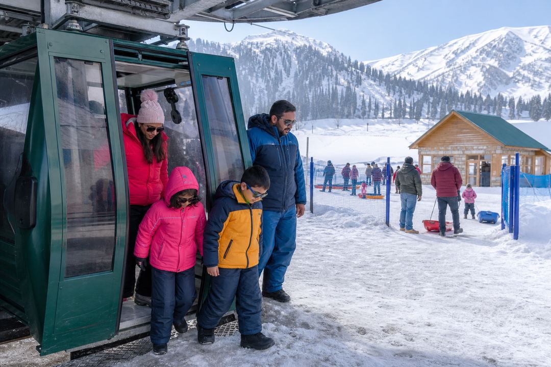 Indian family in winter clothing stepping out of a gondola cabin at Kongdori station with snow and mountain views around them.