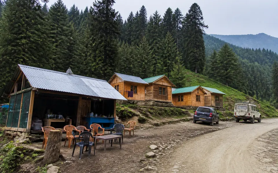 Simple wooden tourist huts and a small roadside tea stall in a forest clearing in Kashmir