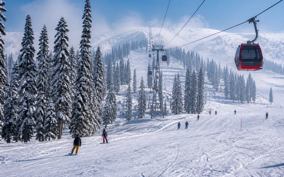 Gulmarg in winter covered in deep snow with pine trees, ski slopes and a cable car visible.