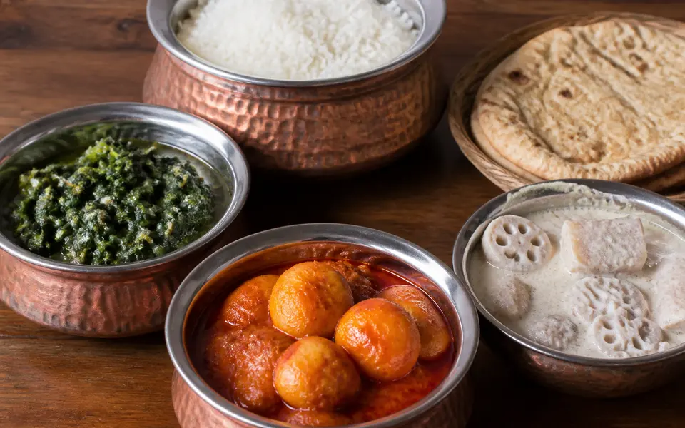 A Kashmiri vegetarian spread with bowls of haak saag, Kashmiri dum aloo, nadru yakhni and rice on a wooden table.