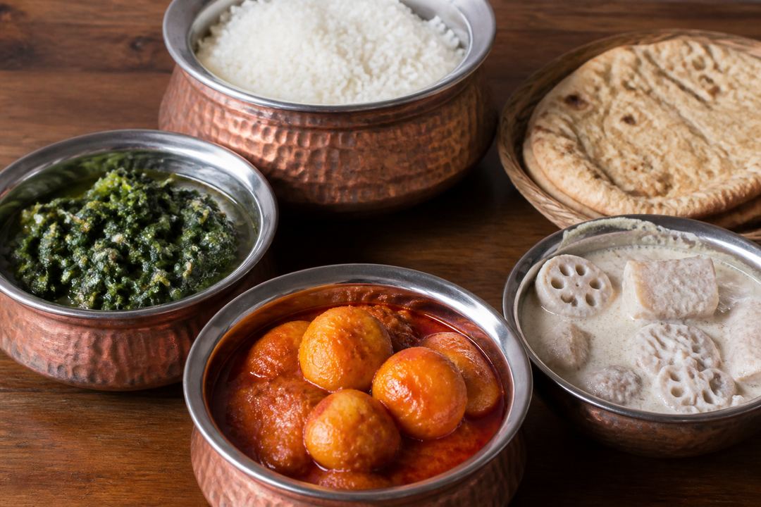 A Kashmiri vegetarian spread with bowls of haak saag, Kashmiri dum aloo, nadru yakhni and rice on a wooden table.