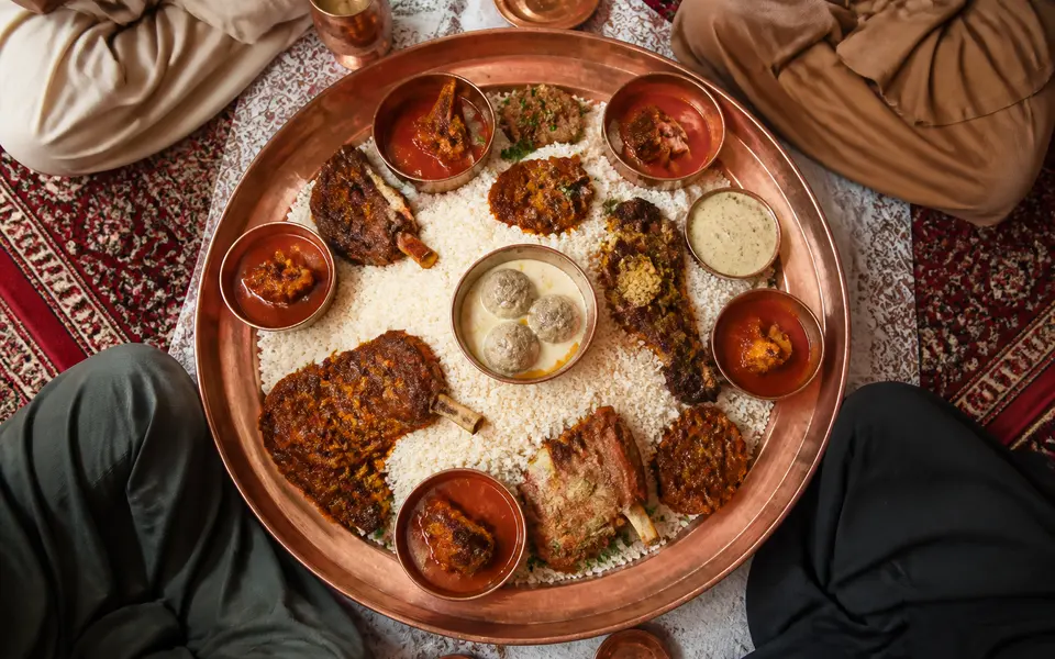 Shared Kashmiri wazwan-style platter on a large metal traem with rice and several meat dishes, surrounded by four diners.
