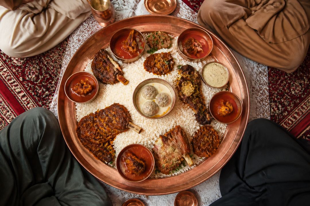 Shared Kashmiri wazwan-style platter on a large metal traem with rice and several meat dishes, surrounded by four diners.