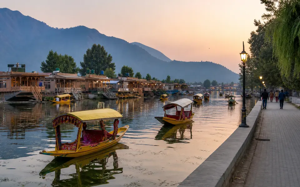 Shikaras on Dal Lake near Boulevard Road at dusk with houseboats, reflections on the water and hills in the background.