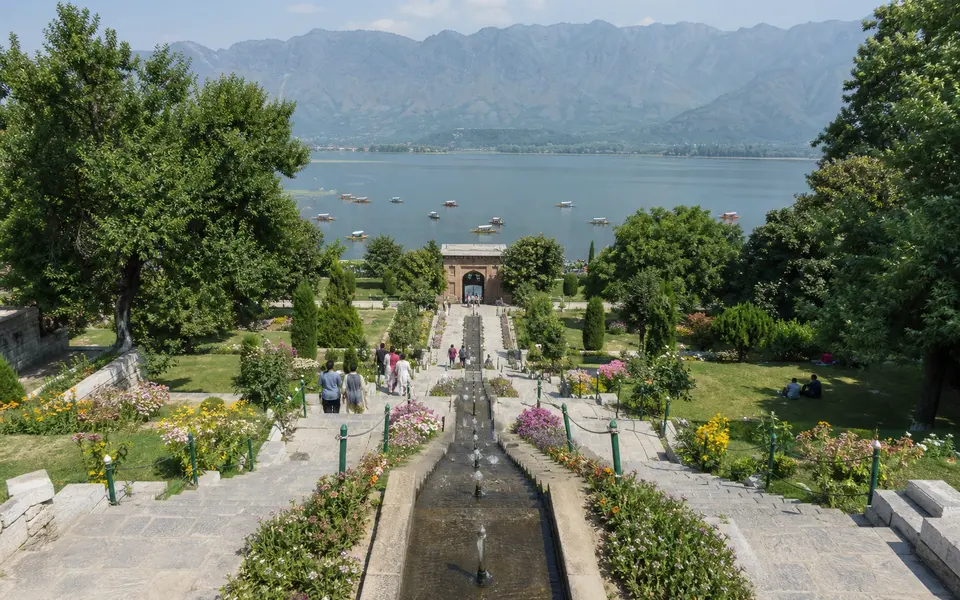 Terraced Mughal garden in Srinagar with stone steps, flower beds, water channels and a view of Dal Lake and the Zabarwan hills.