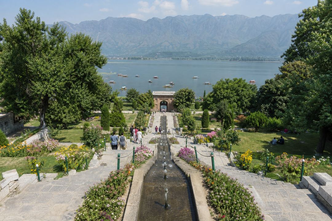 Terraced Mughal garden in Srinagar with stone steps, flower beds, water channels and a view of Dal Lake and the Zabarwan hills.