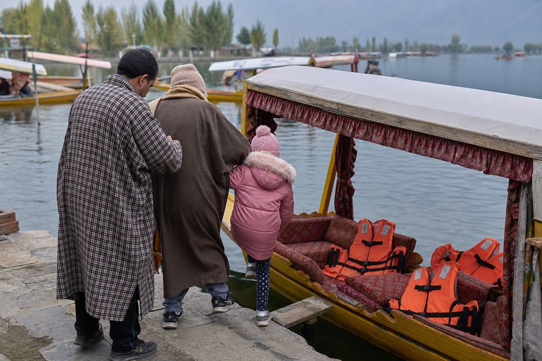 Boatman helping a family board a shikara on Dal Lake, with life jackets visible on the boat.