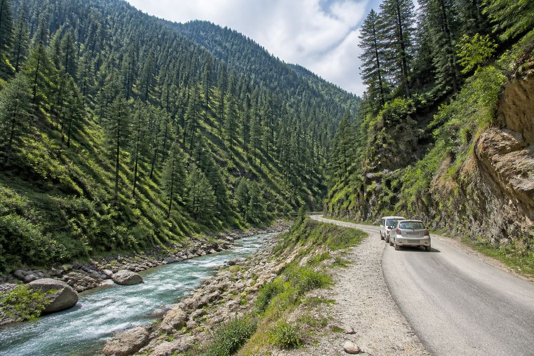 Forested mountain valley with a small road and river, similar to the landscape around Daksum in south Kashmir