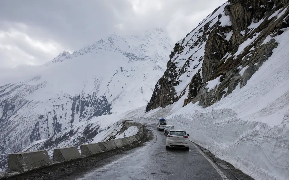 High mountain road near Sonamarg with sharp bends, snow walls at the roadside and a few vehicles driving towards a high pass.