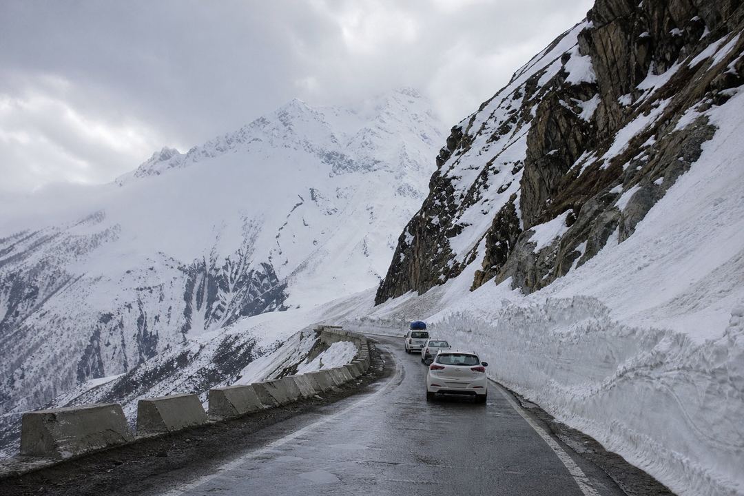 High mountain road near Sonamarg with sharp bends, snow walls at the roadside and a few vehicles driving towards a high pass.
